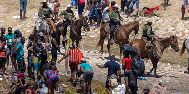 CIUDAD ACUNA, MEXICO - SEPTEMBER 20: Mounted U.S. Border Patrol agents watch Haitian immigrants on the bank of the Rio Grande in Del Rio, Texas on September 20, 2021 as seen from Ciudad Acuna, Mexico. As U.S. immigration authorities began deporting immigrants back to Haiti from Del Rio, thousands more waited in a camp under an international bridge in Del Rio while others crossed the river back into Mexico to avoid deportation. 