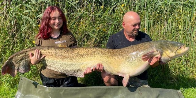 Hannah Truscott (izquierda) y su padre Paul Truscott (derecha) agitan su captura de 96 libras y 4 onzas.  Se dice que el joven de 15 años atrapó el bagre gigante en los lagos blancos del condado de Essex.