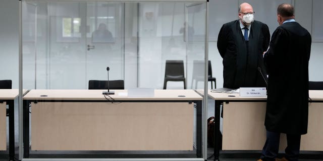 Two lawmakers stand next to an empty seat of the accused at the courtroom, prior to a trial against a 96-year-old former secretary for the SS commander of the Stutthof concentration camp at the court in Itzehoe, Germany, Thursday, Sept. 30, 2021. The woman is charged of more than 11,000 counts of accessory to murder. Prosecutors argue that the 96-year-old woman was part of the apparatus that helped the Nazi camp function more than 75 years ago.(AP Photo/Markus Schreiber, Pool)