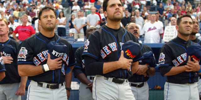 # 47 left fielder Joe McEwing, # 4 John Valentin shortstop, # 31 wide receiver Mike Piazza, # 13 third baseman Edgardo Alfonzo and # 20 Mets right fielder Jeromy Burnitz. New Yorkers hold their FDNY and NYPD hats over their hearts during the national anthem ahead of Game 2 of an MLB brace against the Atlanta Braves on September 11, 2002 at Turner Field in Atlanta, Georgia. The Mets shut out the Braves 5-0.