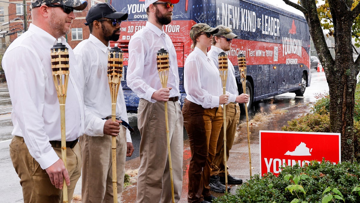 A small group of demonstrators dressed as "Unite the Right" rally-goers with tiki torches stand on a sidewalk as Republican candidate for governor of Virginia Glenn Youngkin arrives on his bus for a campaign event at a Mexican restaurant in Charlottesville, Virginia, Oct. 29, 2021. 