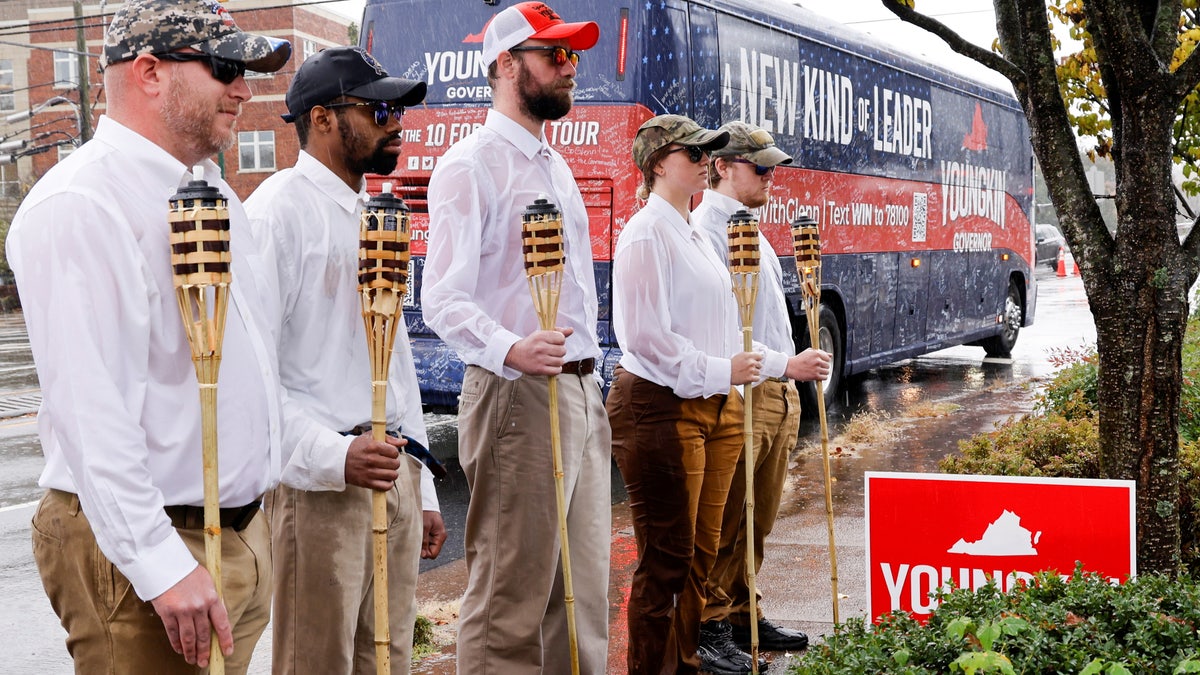 A small group of demonstrators dressed as "Unite the Right" rally-goers with tiki torches stand on a sidewalk as Republican candidate for governor of Virginia Glenn Youngkin arrives on his bus for a campaign event at a Mexican restaurant in Charlottesville, Virginia, U.S. October 29, 2021. REUTERS/Jonathan Ernst