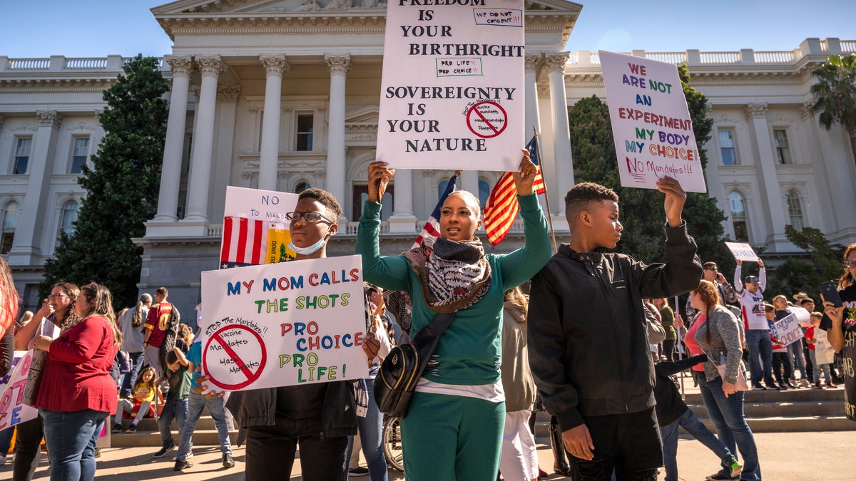Lakita Strong, center, holds a sign protesting mandatory COVID-19 vaccinations for schoolchildren with her sons Jordan, left, and Jayden, right, at the state Capitol in Sacramento, Calif., Monday, Oct. 18, 2021. (Hector Amezcua/The Sacramento Bee via AP)