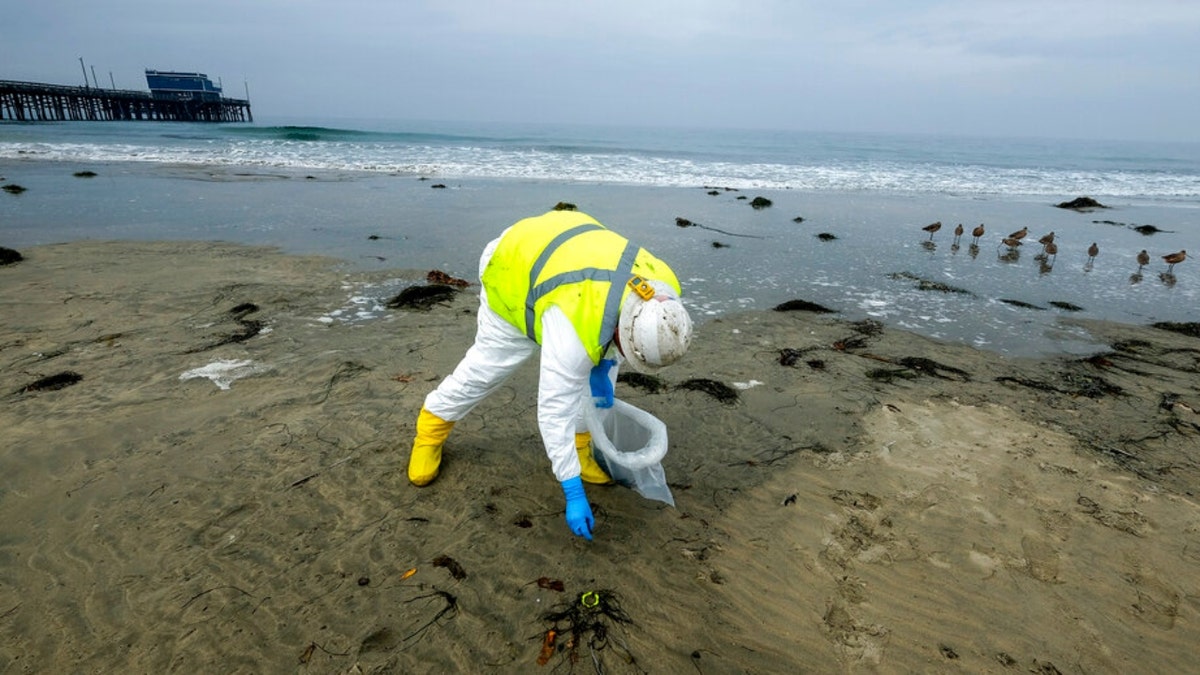 A worker in protective suit cleans the contaminated beach after an oil spill in Newport Beach, Calif., on Thursday, Oct. 7, 2021. More than five days after an offshore pipeline ruptured off the Southern California coast, there’s still no confirmation of exactly how much oil has spilled into the ocean. 