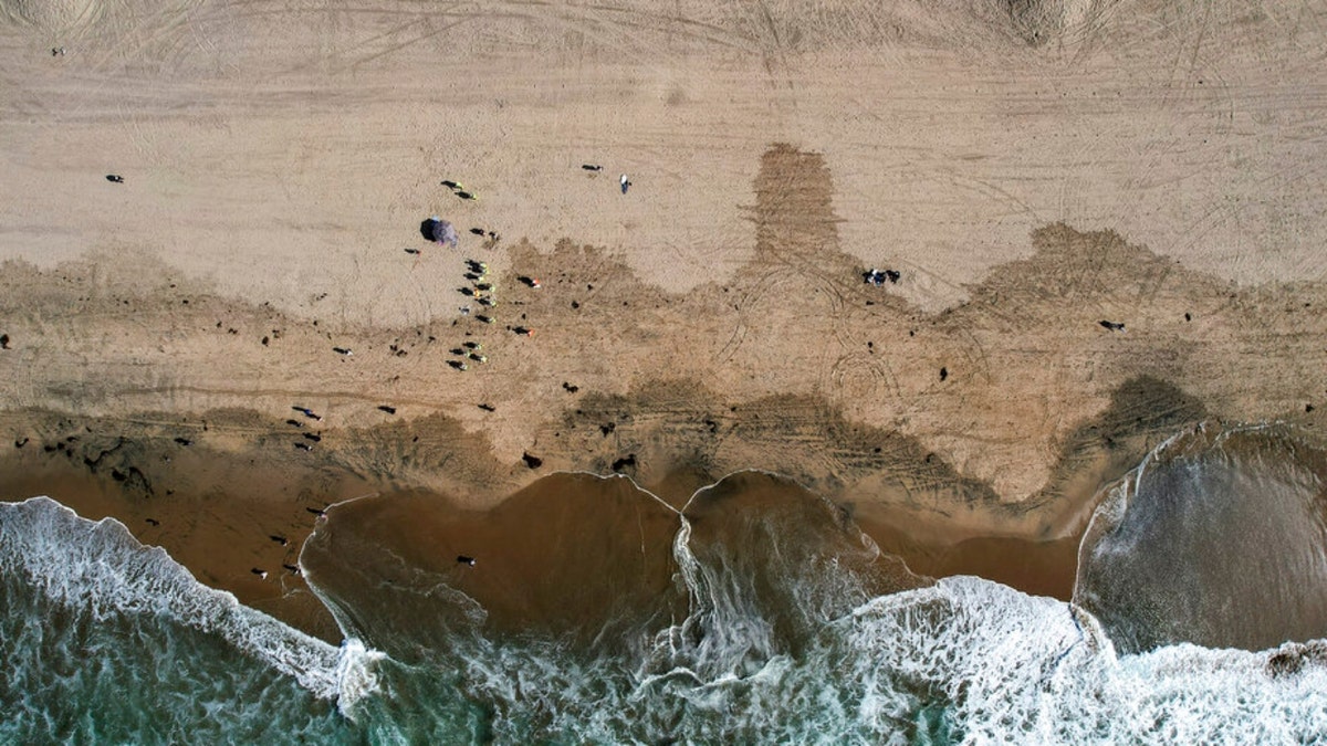 In this aerial image taken with a drone, beach goers are seen as workers in protective suits continue to clean the contaminated beach in Huntington Beach, Calif., Monday, Oct. 11, 2021. Huntington Beach reopened its shoreline this morning after water testing results came back with non-detectable amounts of oil associated toxins in ocean water, city officials and California State Parks announced. 