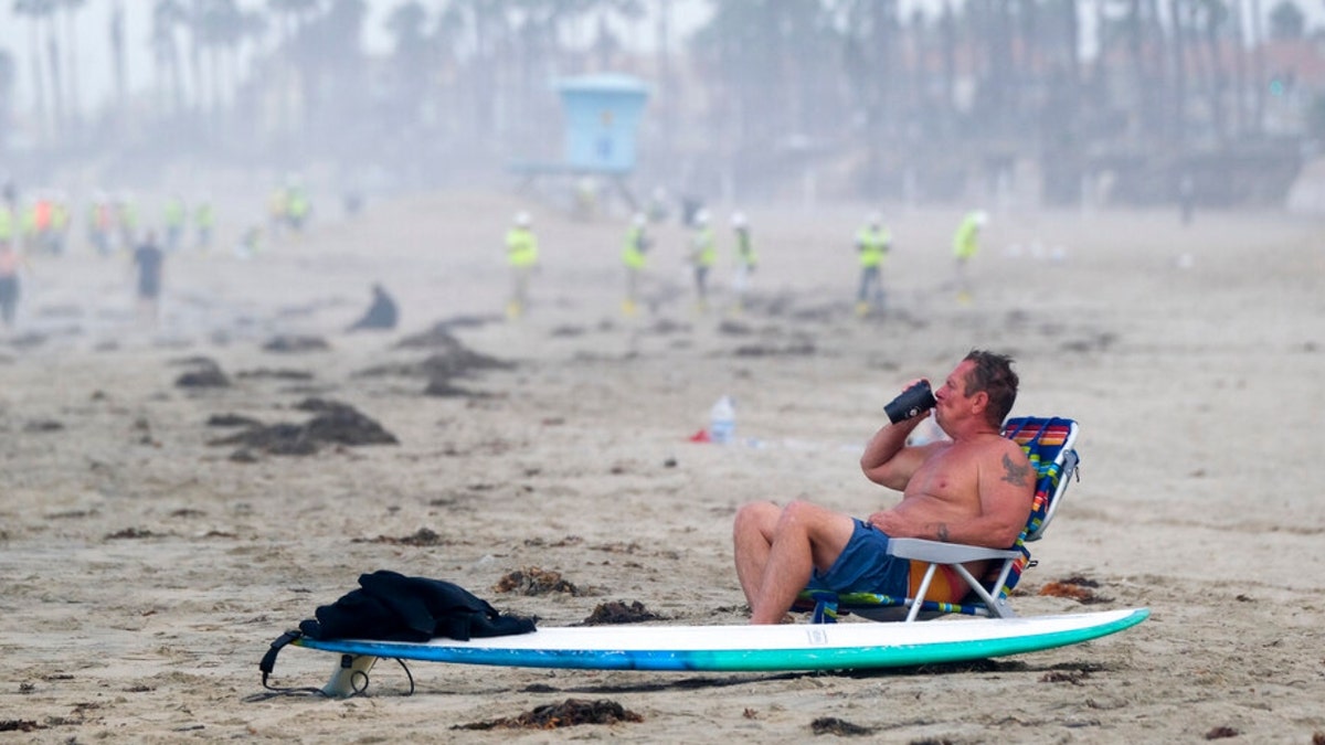 A man rests as workers in protective suits continue to clean the contaminated beach in Huntington Beach, Calif., Monday, Oct. 11, 2021. Huntington Beach reopened its shoreline this morning after water testing results came back with non-detectable amounts of oil associated toxins in ocean water, city officials and California State Parks announced. 