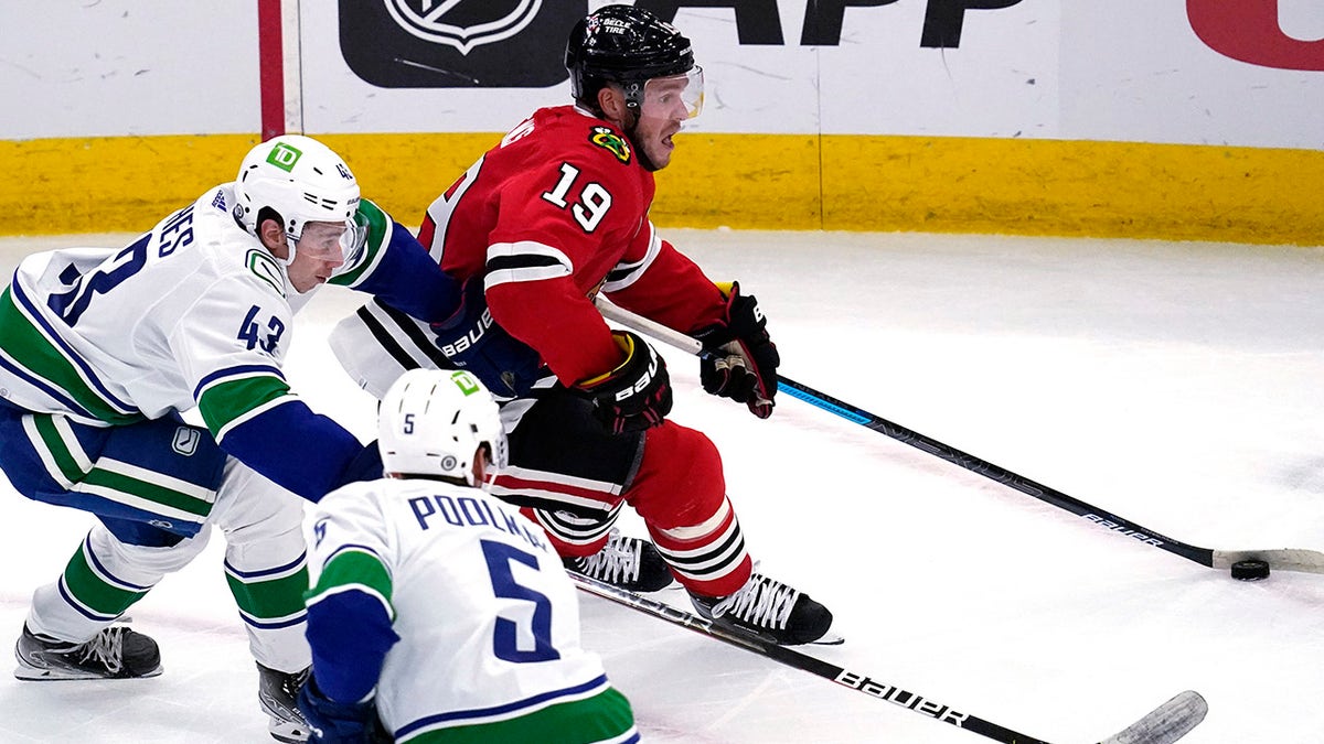 Chicago Blackhawks center Jonathan Toews (19) controls the puck against Vancouver Canucks defenseman Quinn Hughes (43) and defenseman Tucker Poolman during the second period of an NHL hockey game in Chicago, Thursday, Oct. 21, 2021.