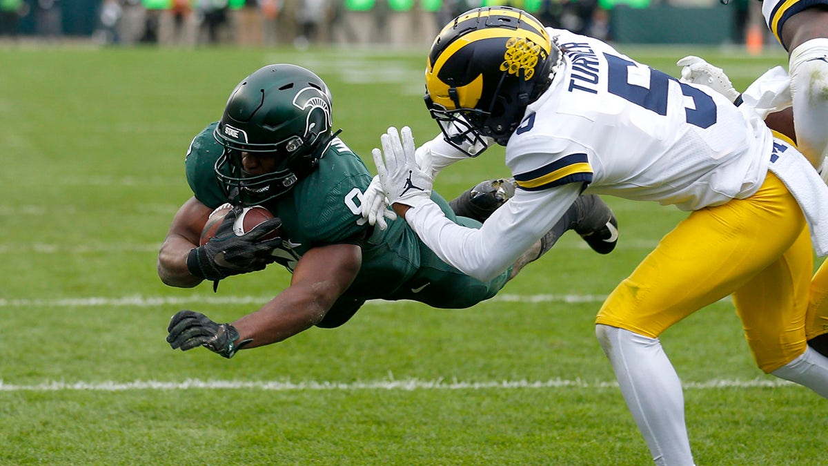 Michigan State's Kenneth Walker III, left, dives over the goal line for a touchdown against Michigan's DJ Turner during the second quarter Saturday, Oct. 30, 2021, in East Lansing, Mich.