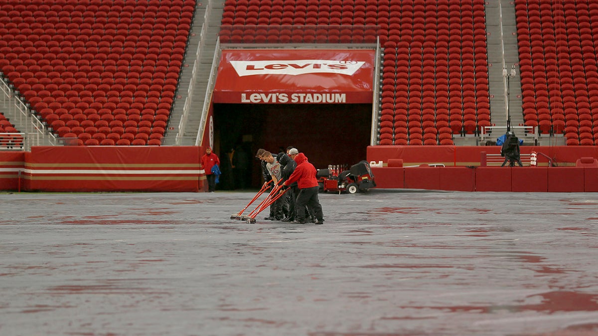Workers push water off a tarp covering the field from rain at Levi's Stadium before an NFL football game between the San Francisco 49ers and the Indianapolis Colts in Santa Clara, Calif., Sunday, Oct. 24, 2021. A powerful storm roared ashore Sunday in Northern California, flooding highways, toppling trees and causing mud flows as forecasters predict record-breaking rainfall.