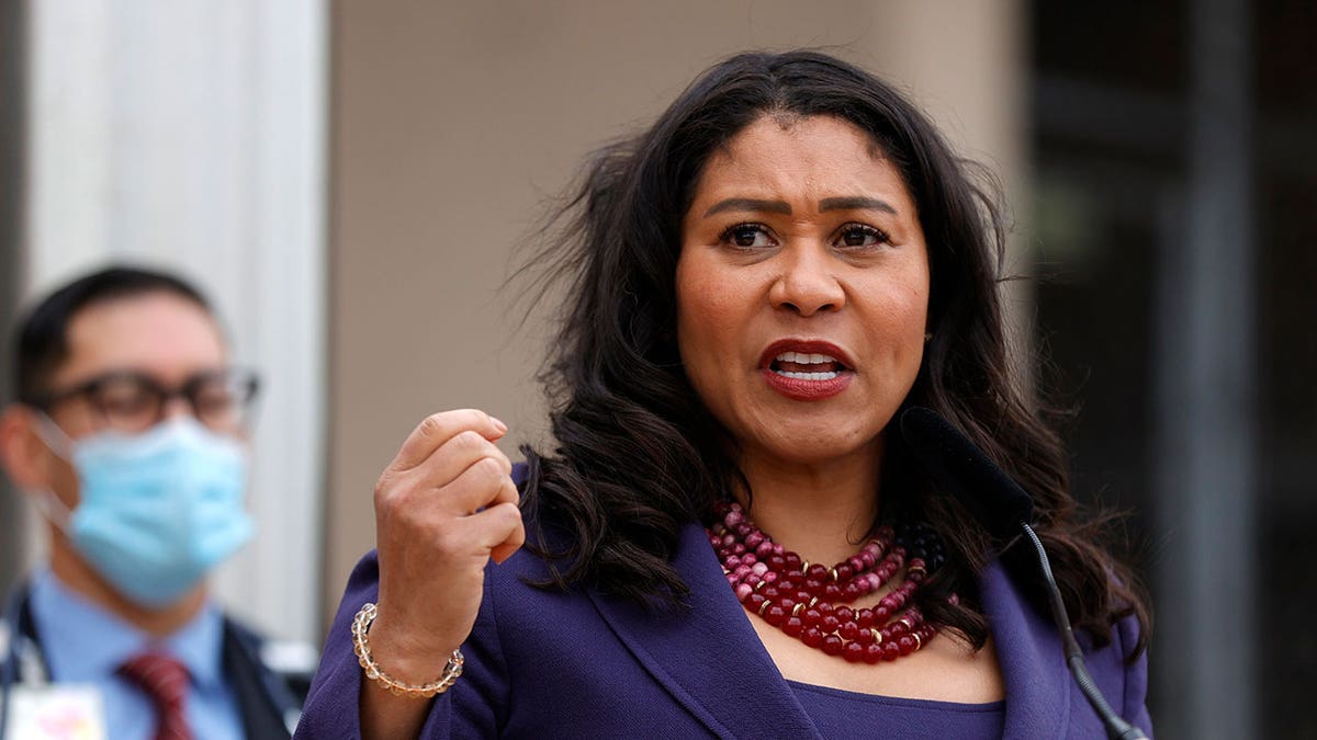 Mayor London Breed seen in photo raising her right hand while addressing the public