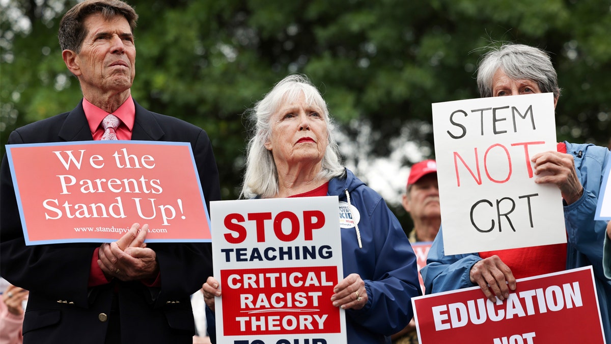 Photo shows a woman holding a sign reading "stop teaching critical race theory" in Loudoun County, VA