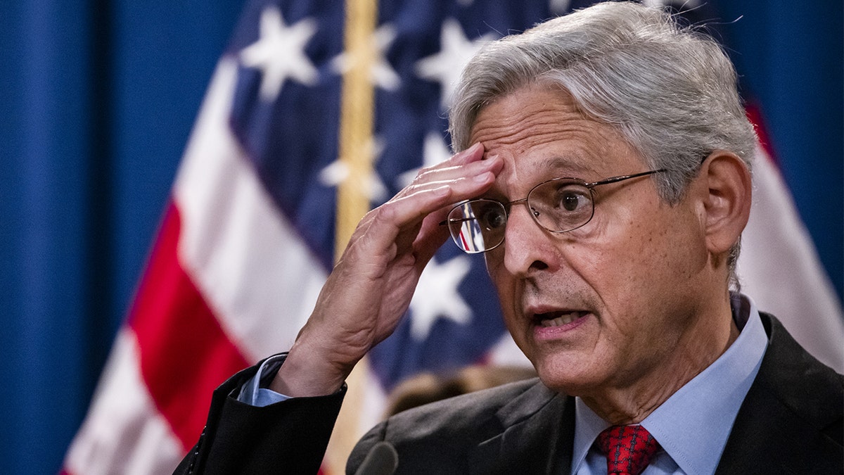 Merrick Garland, hand on forehead, US flag in background