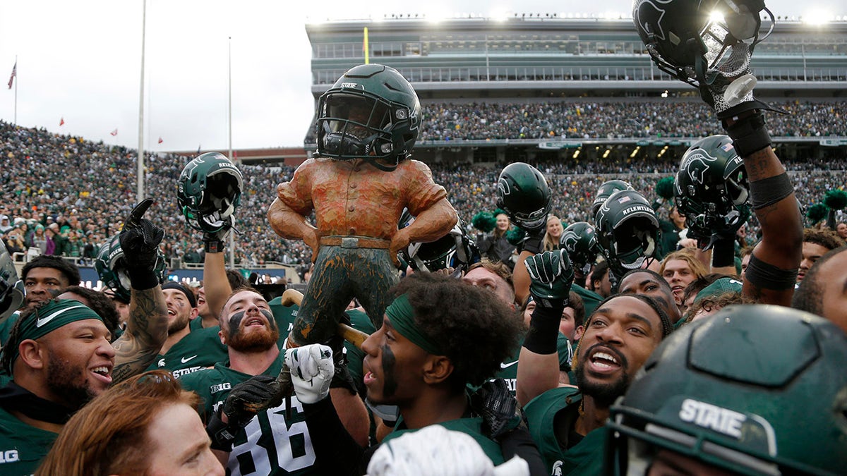 Michigan State players celebrate with the Paul Bunyan trophy defeating Michigan in an NCAA college football game, Saturday, Oct. 30, 2021, in East Lansing, Mich. Michigan State won 37-33. 