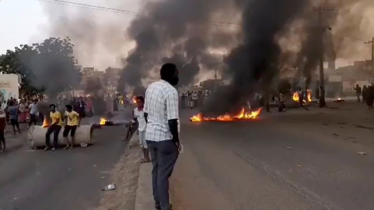 People gathering as fire and smoke are seen on the streets of Kartoum, Sudan, amid reports of a coup Monday.