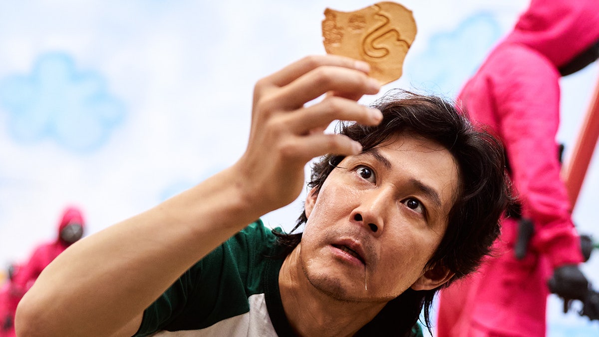 The third episode of the South Korean drama is titled "The Man With the Umbrella." Here, you see the show's protagonist Seong Gi-hun (played by Lee Jung-jae) examining his dalgona candy piece, which has an umbrella printed on it.