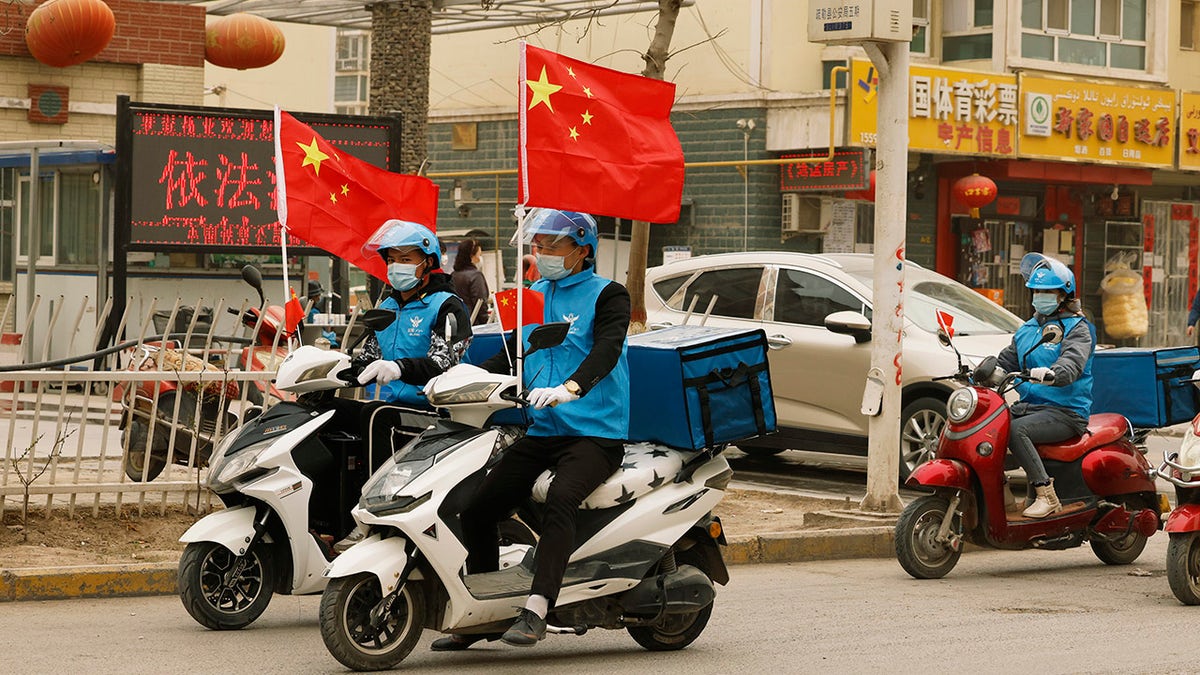 Delivery workers flying Chinese national flags ride around in a convoy to promote their services in Shule county in northwestern China's Xinjiang Uyghur Autonomous Region on March 20, 2021.