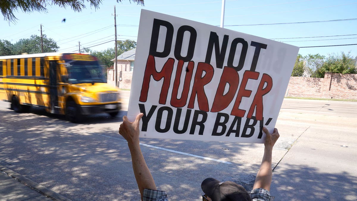 A man is shown holding a sign as a school bus drives by on the street in front of a building housing an abortion provider in Dallas, Texas, on Oct. 7, 2021. 
