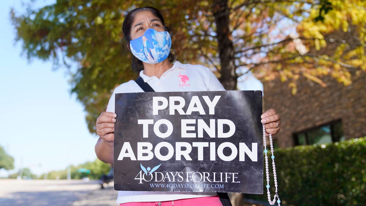 Maria Peña holds a rosary and sign outside a building housing an abortion provider in Dallas, Thursday, Oct. 7, 2021. (AP Photo/LM Otero)