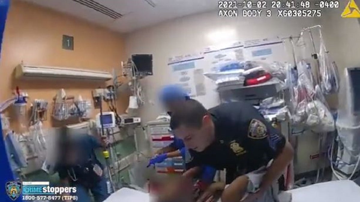 An NYPD officer holds a child and lays him down in a Brooklyn hospital.