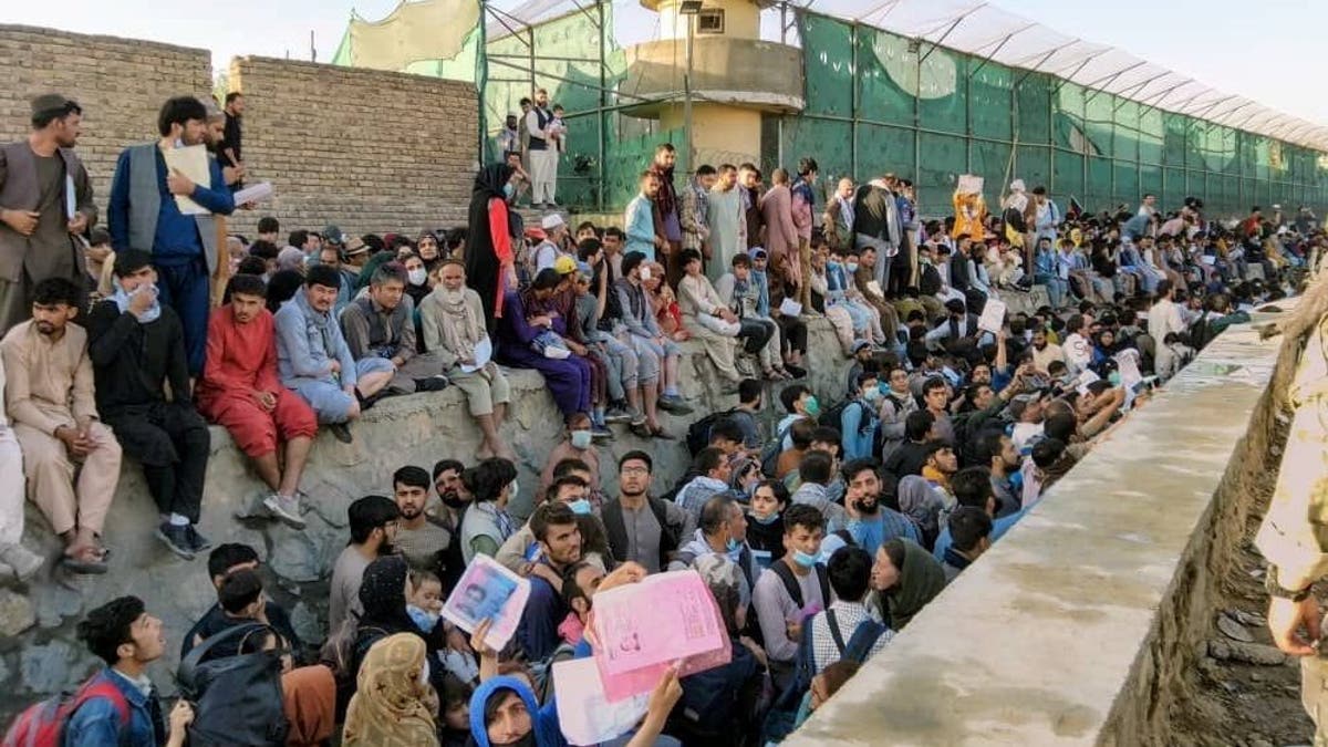 Afghans sitting, standing, and waiting crowd the Kabul airport, standing near a fence