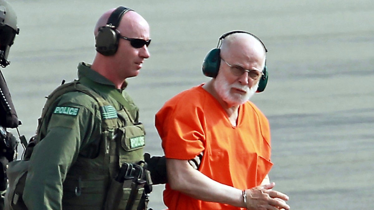 Whitey Bulger con auriculares y un mono de prisión mientras lo escoltan desde un helicóptero de la Guardia Costera de EE. UU.