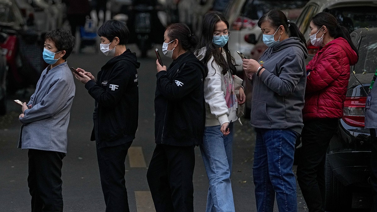 A woman wearing a face mask to help curb the spread of the coronavirus walks through a line of masked service sector women waiting to receive a swab for the COVID-19 test during a mass testing in Beijing on Friday, following a spike of the coronavirus in the capital and other provincials.