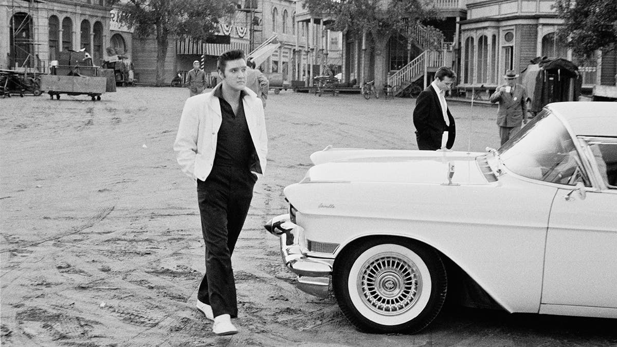 American rock 'n' roll singer and actor Elvis Presley (1935 - 1977) walking past a Cadillac Eldorado on a movie set, USA, circa 1958. Recently, someone stole a bust of the singer from a saloon in central Illinois.