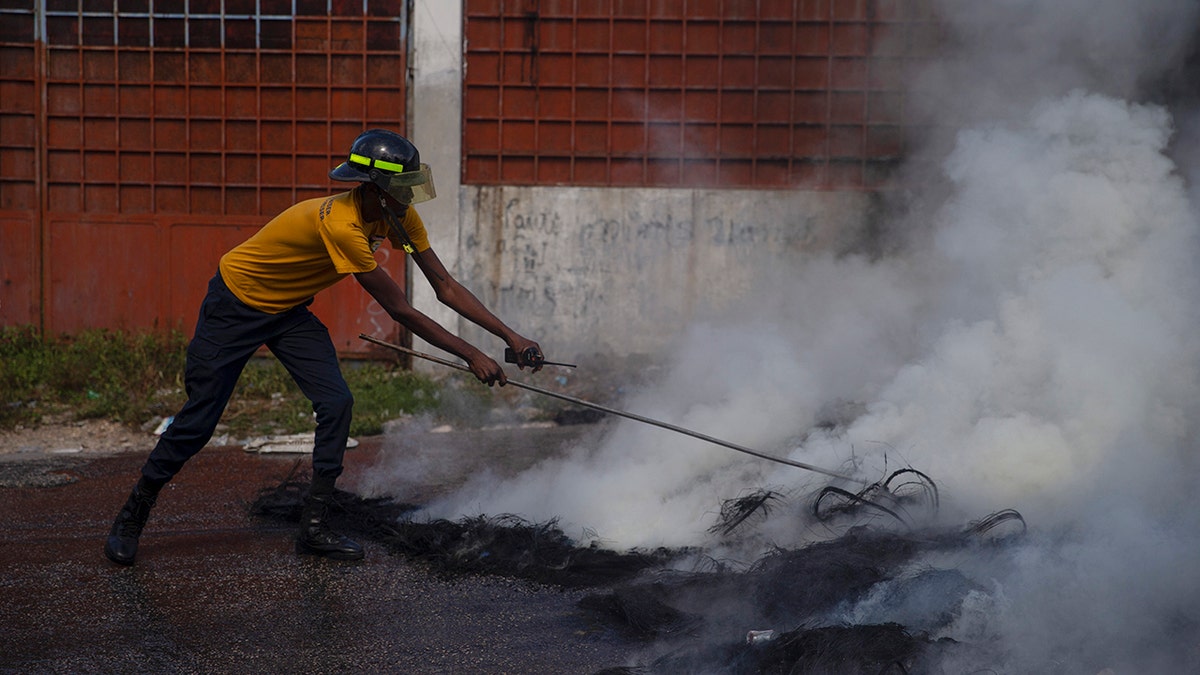 A firefighter puts out a smoldering road block set by protesters in Port-au-Prince, Haiti, on Monday. 