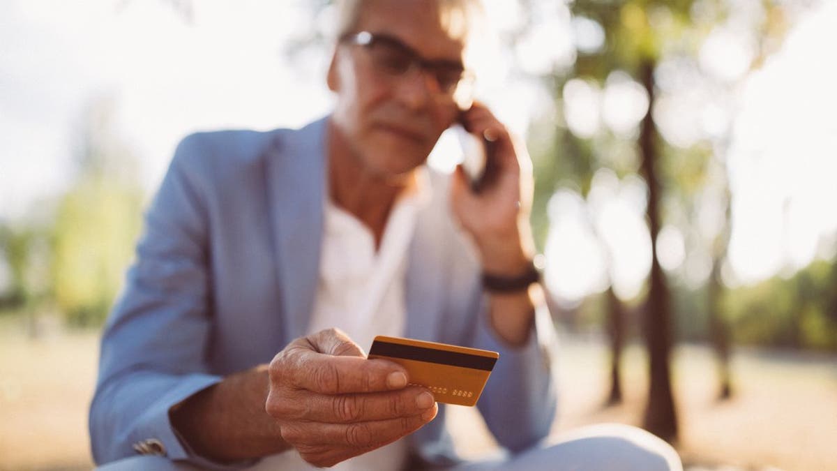 Businessman outside holding credit card and using smartphone