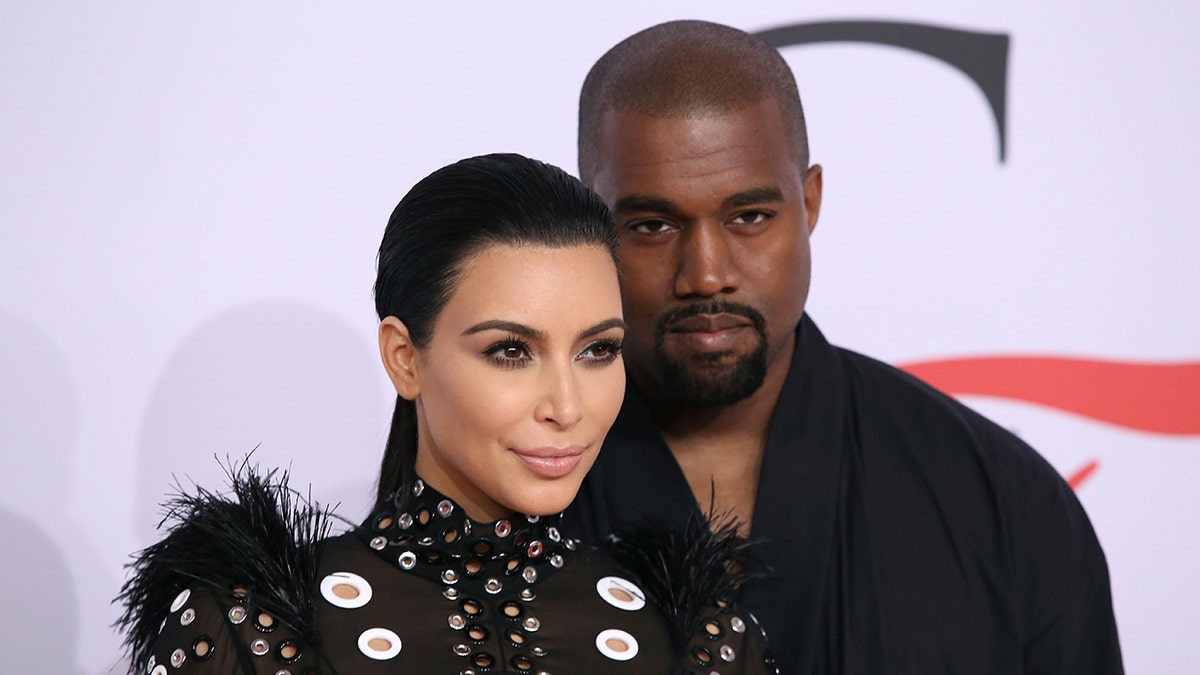 Kim Kardashian in a black dress soft smiles with Kanye West on the carpet