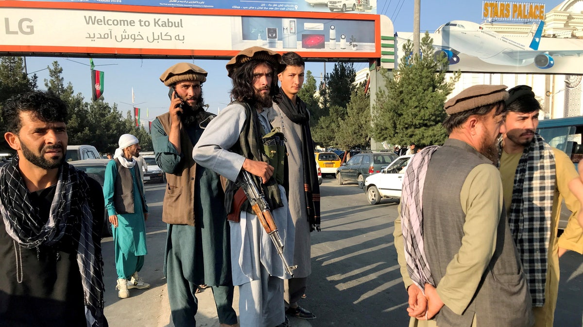 Taliban fighter stands in front of Kabul sign.
