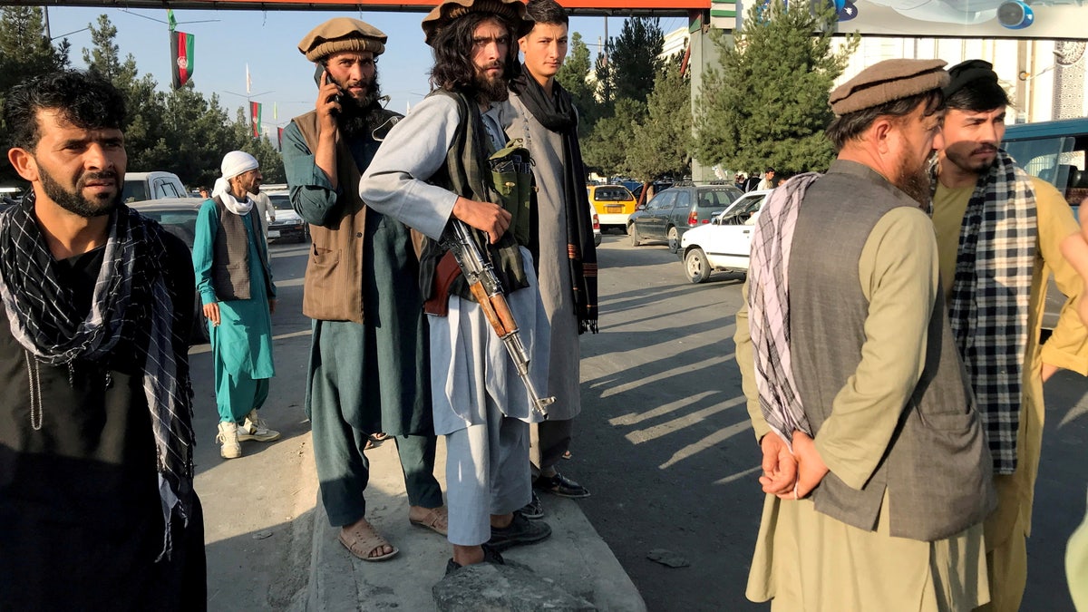 Taliban fighter stands in front of Kabul sign.