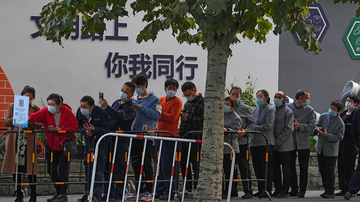 Service sector workers line up for a COVID-19 test during a mass testing at a site baring the words, "You and me on the road of civilization" in Beijing on Friday, following a spike of the coronavirus in the capital and other provinces.
