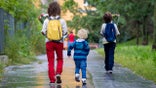 Happy school children, holding bouquet of flowers, going to school first day, rainy autumn day in september
