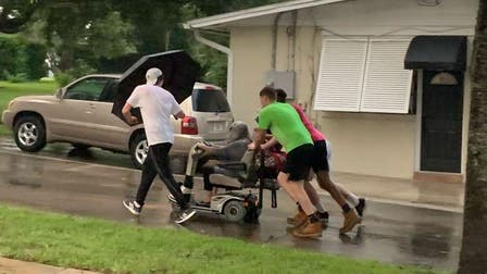 4 young men push elderly woman in broken scooter home in pouring rain