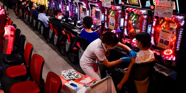 DOSSIER - Dans cette photo d'archive du 13 septembre 2021, une femme reçoit la première injection du vaccin Moderna COVID-19 alors que d'autres attendent leur tour devant des flippers pachinko au salon de pachinko Freedom à Osaka, dans l'ouest du Japon. Presque du jour au lendemain, le Japon est devenu une réussite étonnante et quelque peu mystérieuse de coronavirus. Le nombre de cas est en baisse, mais les experts craignent que, sans savoir exactement comment cela a réduit les cas de manière aussi drastique, la nation pourrait être en réserve pour une autre vague dévastatrice comme pendant l'été. (Kyodo News via AP, Fichier)