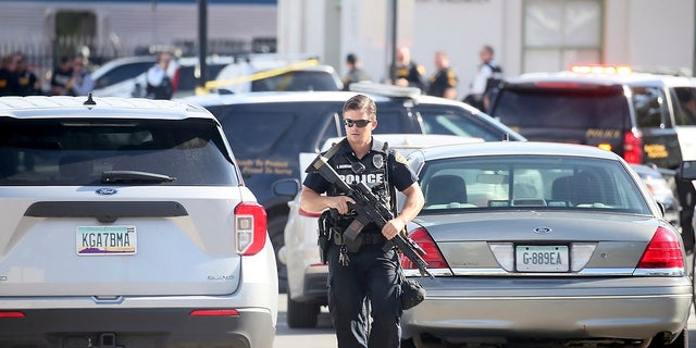 A Tucson Police Department officer walks with his gun near the scene of an Amtrak train shooting in downtown Tucson, Ariz. On Monday where a DEA officer and suspect were been left dead.  (Mamta Popat / Arizona Daily Star via AP)