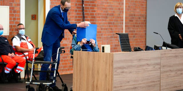 Lawyer Stefan Waterkamp covers the face of accused Josef S. as the arrive at the court room in Brandenburg, Germany, Thursday, Oct. 7, 2021. The 100-year-old man charged as an accessory to murder on allegations that he served as a guard at the Nazis' Sachsenhausen concentration camp during World War II. (AP Photo/Markus Schreiber)