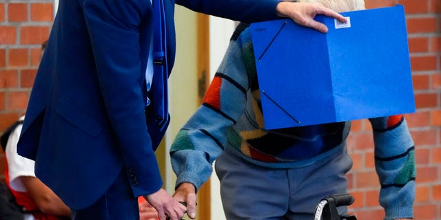 Lawyer Stefan Waterkamp covers the face of accused Josef S. as they arrive at a courtroom in Brandenburg, Germany, Thursday, Oct. 7, 2021. The 100-year-old man is charged as an accessory to murder on allegations that he served as a guard at the Nazis' Sachsenhausen concentration camp during World War II.