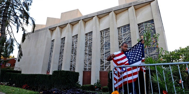 In this Oct. 27, 2019 file photo a man places an American flag outside the Tree of Life synagogue in Pittsburgh on the first anniversary of the shooting at the synagogue, that killed 11 worshippers. An evidentiary hearing in the case of Robert Bowers a western Pennsylvania truck driver accused of killing 11 people at the Pittsburgh synagogue in 2018, is expected to get underway inside a federal courtroom in Pittsburgh on Tuesday.