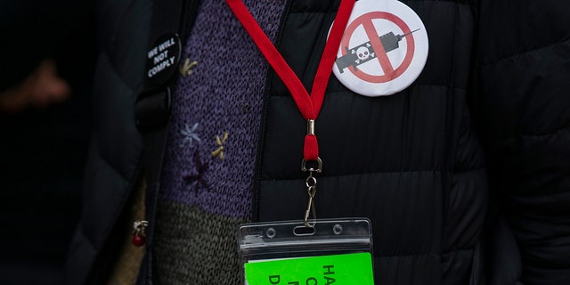 A woman wears an anti-vaccine pin while people and teachers pray as they protest against COVID-19 vaccine mandates outside the Manhattan Federal Court Tuesday, Oct. 12, 2021, in New York City. 