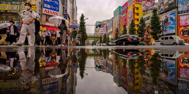 DOSSIER - Dans cette photo d'archive du 12 octobre 2021, des personnes portant des masques de protection se reflètent dans une flaque d'eau alors qu'elles traversent une rue d'un quartier commerçant de Tokyo. Presque du jour au lendemain, le Japon est devenu une réussite étonnante et quelque peu mystérieuse de coronavirus. Le nombre de cas est en baisse, mais les experts craignent que, sans savoir exactement comment cela a réduit les cas de manière aussi drastique, la nation pourrait être en réserve pour une autre vague dévastatrice comme pendant l'été. (AP Photo/Kiichiro Sato, dossier)