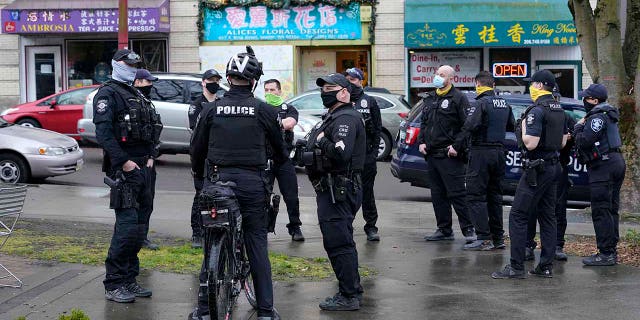 Seattle Police officers confer after taking part in a public roll call at Hing Hay Park in Seattle's Chinatown-International District Thursday, March 18, 2021.