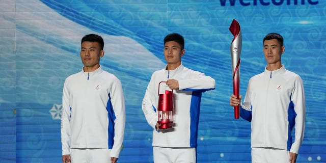 Volunteers hold the Olympic torch and the frame on stage during a welcome ceremony for the Frame of Olympic Winter Games Beijing 2022, held at the Olympic Tower in Beijing, Wednesday, Oct. 20, 2021. A welcome ceremony for the Olympic flame was held in Beijing on Wednesday morning after it arrived at the Chinese capital from Greece.  (AP Photo/Andy Wong)