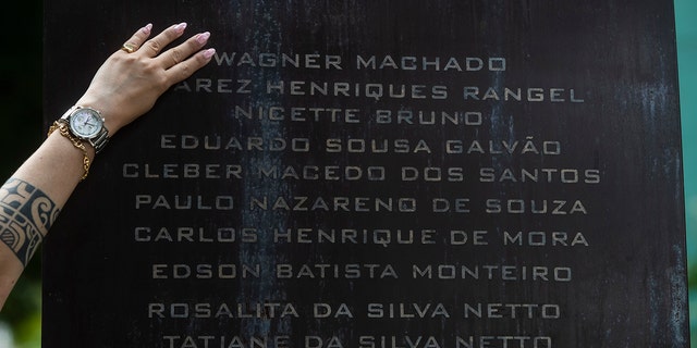 에리카 데 바스콘셀로스 마차도(40)가 리오 데 카호 지역 화장터와 묘지에서 가족을 위로하고 코로나19로 사망한 사람들을 기리기 위해 설치된 인 베네토 기념관에 새겨진 아버지의 이름에 손을 얹고 있다. 2021년 10월 27일 수요일, 브라질 자네이루. 