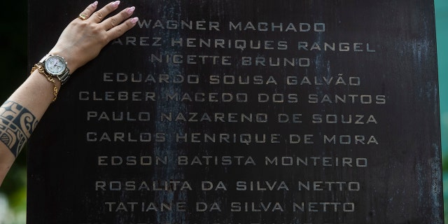 Erika de Vasconcelos Machado, 40, places her hand on her father's name inscribed on the In-Finito Memorial, installed to comfort family members and honor those who died from COVID-19, at the Penitence Crematorium and Cemetery, in the Caju neighborhood of Rio de Janeiro, Brazil, Wednesday, Oct. 27, 2021. 