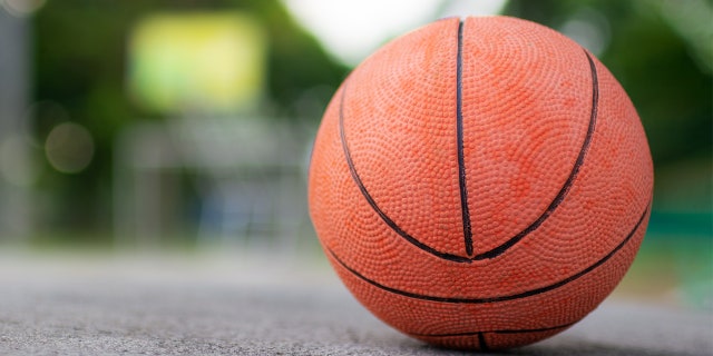 An orange ball placed on a cement floor, ready to play on a basketball court in the park.