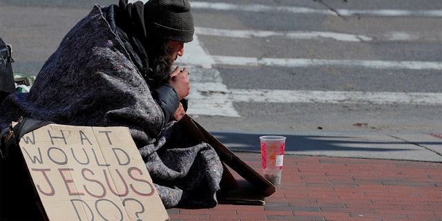 Billy, who has been experiencing homelessness for seven years, sits with a sign reading "What Would Jesus Do?" amid the coronavirus disease outbreak in Boston, April 15, 2020. (REUTERS/Brian Snyder(