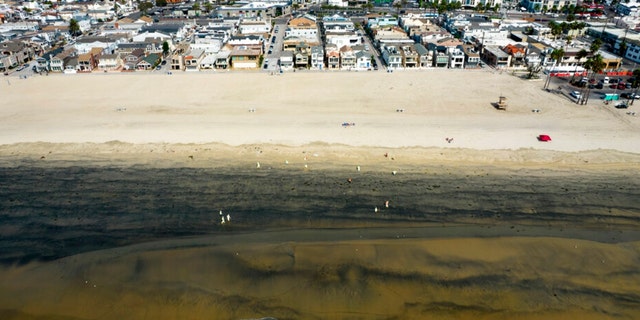 An aerial photo shows workers in protective suits clean the contaminated beach after an oil spill in Newport Beach, Calif., on Wednesday, Oct. 6, 2021. A major oil spill off the coast of Southern California fouled popular beaches and killed wildlife while crews scrambled Sunday, to contain the crude before it spread further into protected wetlands. 