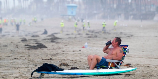 A man rests as workers in protective suits continue to clean the contaminated beach in Huntington Beach, Calif., Monday, Oct. 11, 2021. Huntington Beach reopened its shoreline this morning after water testing results came back with non-detectable amounts of oil associated toxins in ocean water, city officials and California State Parks announced. 